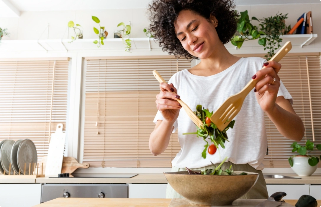 A woman enjoying a salad with a wooden spoon in hand.