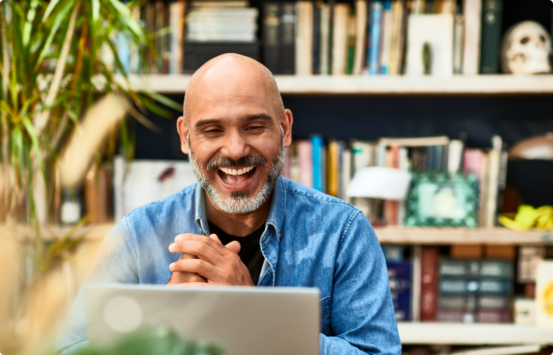 A bald man smiling while using a laptop to work or browse the internet.