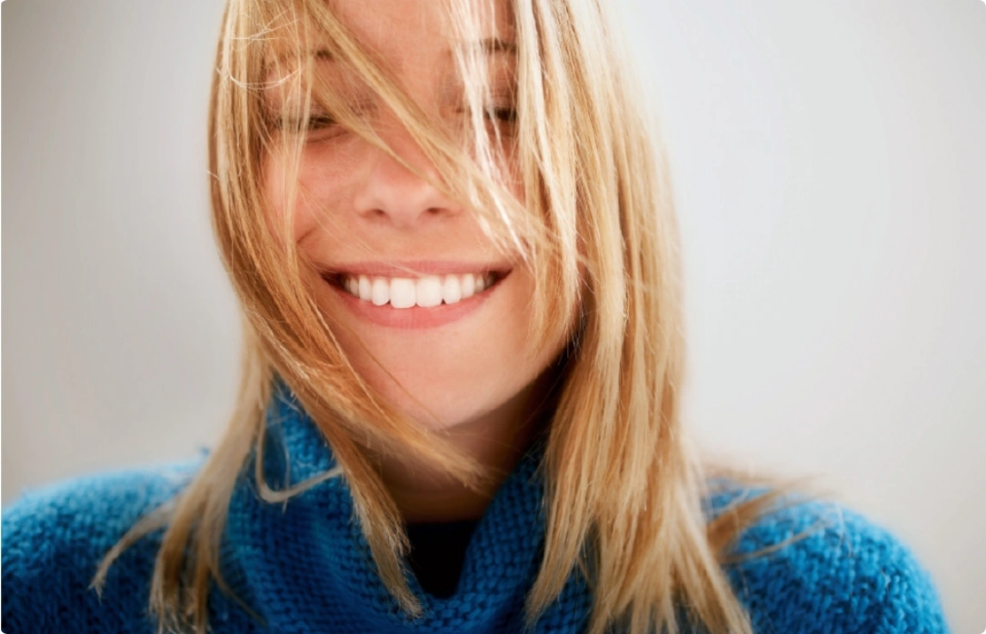 A woman with long blonde hair smiling, radiating warmth and happiness.