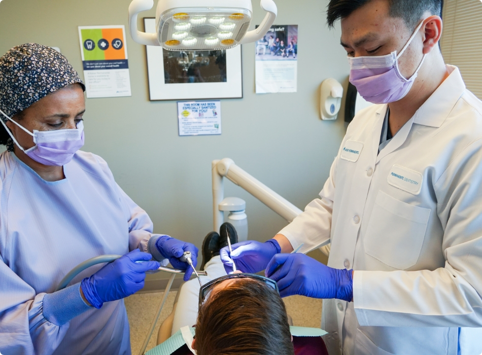 A dentist examining a patient's teeth in a dental office, with dental tools and equipment visible.