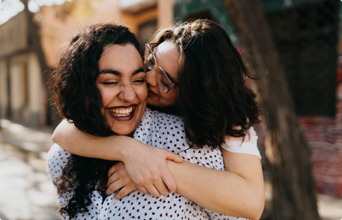 Two women happily embrace each other on a street, radiating joy and warmth through their smiles.