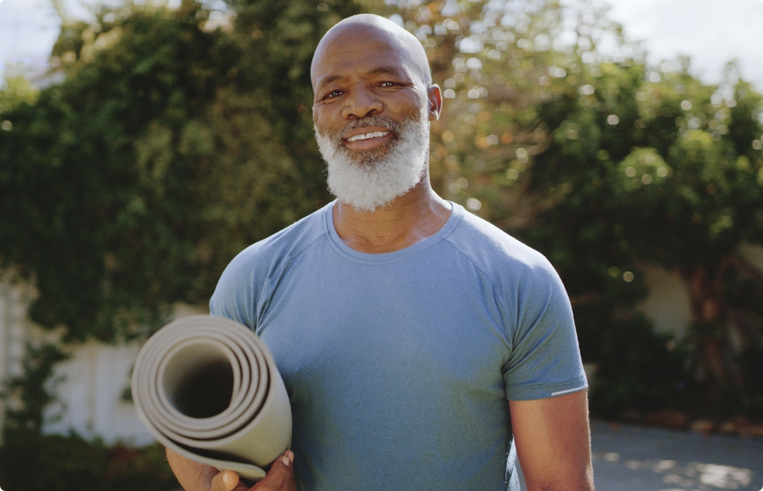 An older man with a beard holding a yoga mat, ready to embark on a peaceful and rejuvenating yoga session.