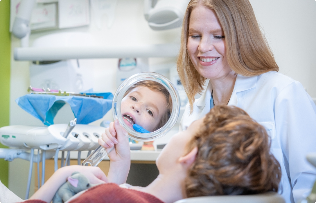 A woman attentively observes a child sitting in a dentist chair during a dental appointment.
