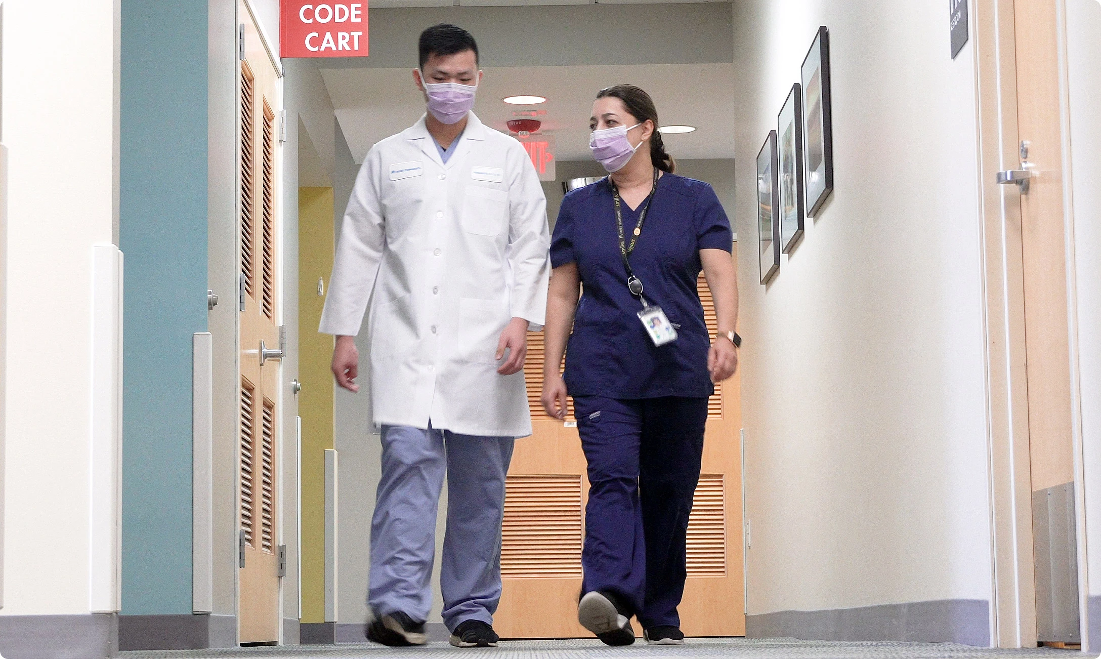 Two individuals wearing face masks walking down a hallway.